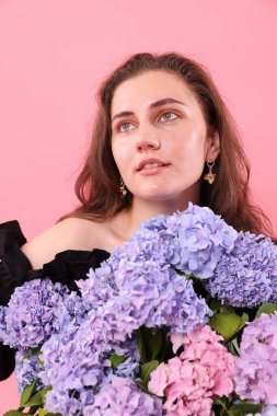 Pembe arka planda Hortensiya çiçekleri olan güzel bir kadın.