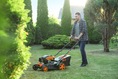 Bahçede çim biçme makinesiyle yeşil çim biçen bir adam