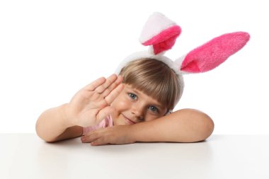 Tavşan kulaklı meraklı küçük kız beyaz arka planda masanın üstünden bakıyor.