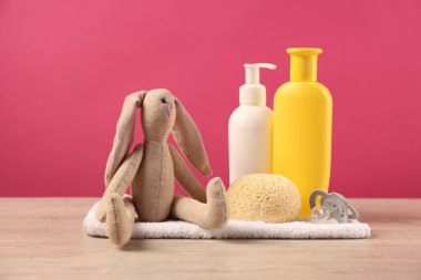 Bebek aksesuarları ve banyo ürünleri pembe arka plana karşı ahşap masada.