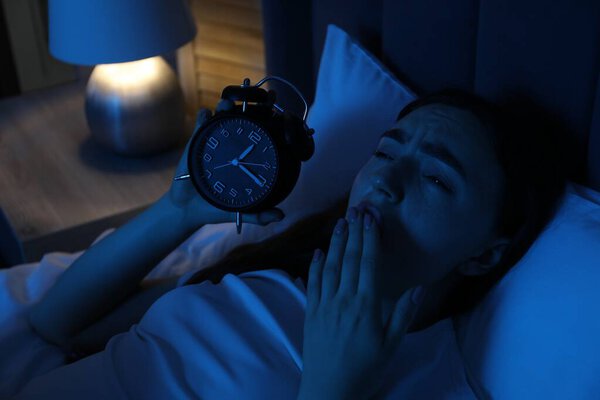 Разочарованная женщина с будильником страдает от бессонницы в постели дома