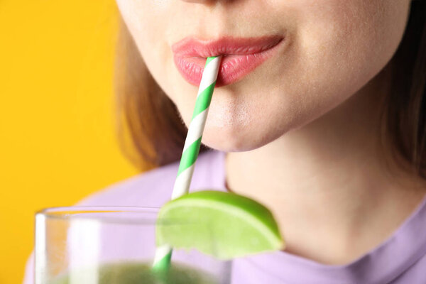 Woman drinking refreshing drink through straw on orange background, closeup