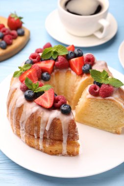 Lezzetli meyveli kek parçaları, açık mavi ahşap masa üzerinde jöle ve nane, yakın plan.