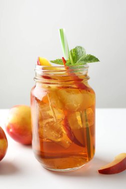 Kavanozda naneli buzlu şeftali çayı ve beyaz masada taze meyveler, yakın plan.