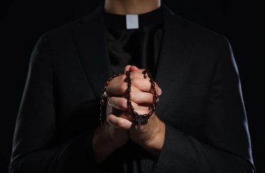 Siyah arka planda tespih çeken rahip, yakın plan.