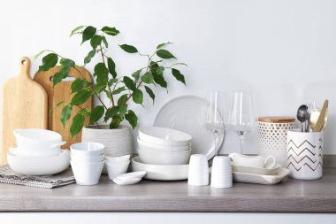 Farklı beyaz bulaşık takımları, ahşap kesim tahtaları, bardaklar, çatal bıçak takımı ve mutfak tezgahında ev bitkisi.