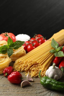 Farklı türde makarna ve malzemeler ahşap masada, yakın plan.