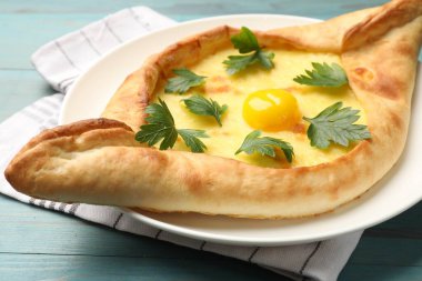 Peynirli, yumurtalı ve maydanozlu leziz khachapuri açık mavi ahşap masa, yakın plan.