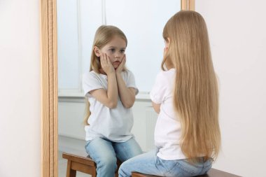 Üzgün küçük kız aynada kendine bakıyor.