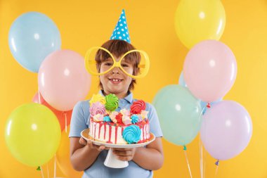 Doğum günü kutlaması. Tatlı ve turuncu arka planda balonları olan tatlı bir çocuk.