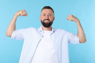 Kuvvet. Gülümseyen adam kaslarını açık mavi arka planda gösteriyor.