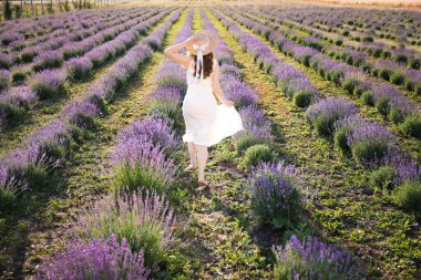 Hasır şapkalı kadın lavanta tarlasında koşuyor.