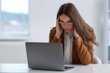 Ofisteki beyaz masada dizüstü bilgisayarı olan üzgün genç bir kadın.