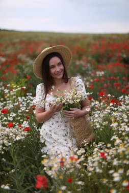 Bir çanta papatya çiçeğiyle gülümseyen kadın çayırda yürüyor.