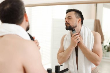 Yakışıklı adam banyoda aynanın yanında tıraş makinesiyle tıraş oluyor.