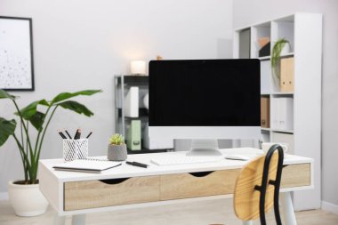 Ofisteki beyaz masa üzerinde modern bilgisayarı ve kırtasiyesi olan şık bir iş yeri.