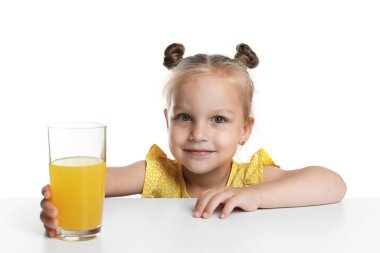 Masada beyaz arka planda bir bardak portakal suyuna uzanan tatlı küçük kız.