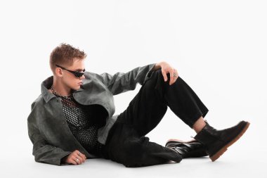 Beyaz arka planda şık ceket ve güneş gözlüğü takan yakışıklı bir genç.