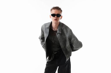 Beyaz arka planda şık ceket ve güneş gözlüğü takan yakışıklı bir genç.
