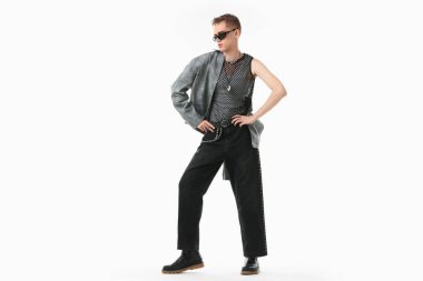 Beyaz arka planda şık ceket ve güneş gözlüğü takan yakışıklı bir genç.