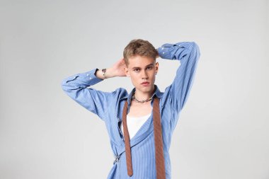 Yakışıklı genç adam açık gri arka planda şık kıyafetler giyiyor.