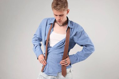 Yakışıklı genç adam açık gri arka planda şık kıyafetler giyiyor.