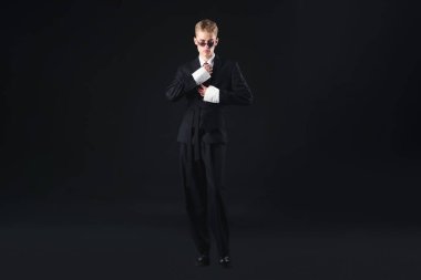 Siyah arka planda şık bir takım elbise ve güneş gözlüğü takan yakışıklı bir genç.