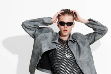 Beyaz arka planda şık ceket ve güneş gözlüğü takan yakışıklı bir genç.