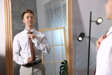 Aynanın yanında aynaya bakarken kravatı ayarlayan yakışıklı bir adam.