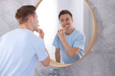 Hazırlanıyor. Evdeki genç adam aynanın yanında dişlerini fırçalıyor.