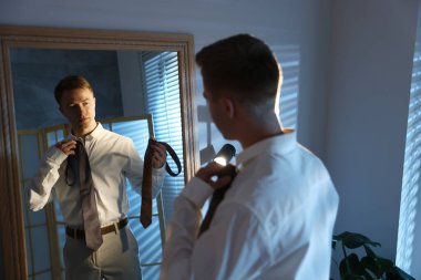 Kapalı alanda aynanın yanında kravat seçen bir adam.