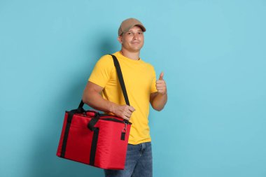 Termo çantalı kurye açık mavi arka planda baş parmak gösteriyor. Yemek dağıtım servisi.