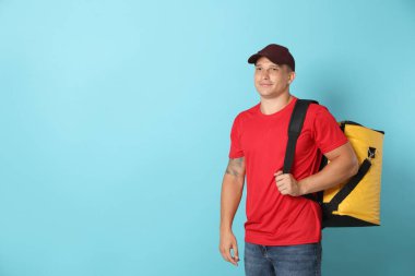 Açık mavi arka planda termo çantalı kurye, mesaj için boşluk. Yemek dağıtım servisi.