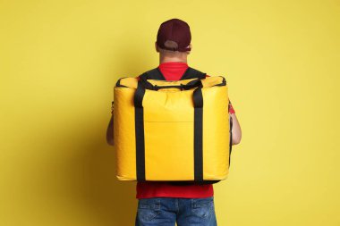 Sarı arka planda termo çantalı bir kurye. Yemek dağıtım servisi.
