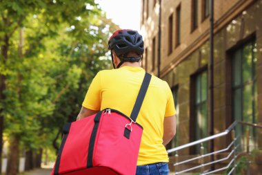 Termo çantalı bir kurye dışarıda bisiklet sürüyor, arkadan bakıyor. Yemek dağıtım servisi.