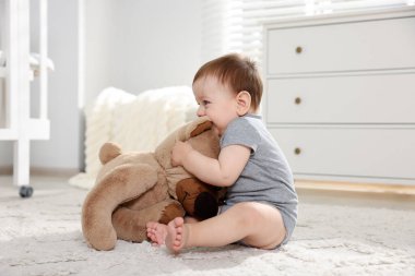 Küçük şirin bebek odada oyuncak ayıyla oynuyor.
