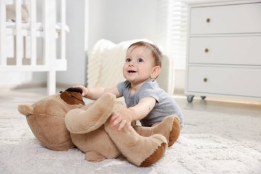 Küçük şirin bebek odada oyuncak ayıyla oynuyor.