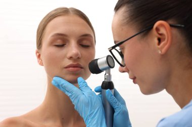 Doktor hastanede dermatoskopla genç kadının benini inceliyor.