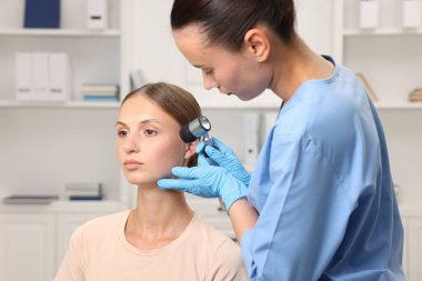 Doktor hastanede dermatoskopla genç kadının benini inceliyor.