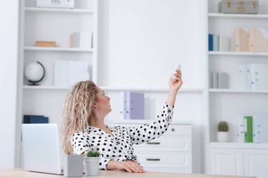 Ofisteki klimayı uzaktan kumandayla kontrol eden kadın