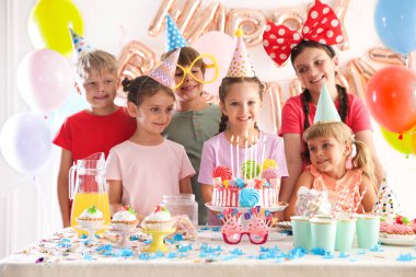 Doğum günü kutlaması. Masadaki çocuklar lezzetli pastalar ve dekoratif odalarda farklı şeyler yiyorlar.