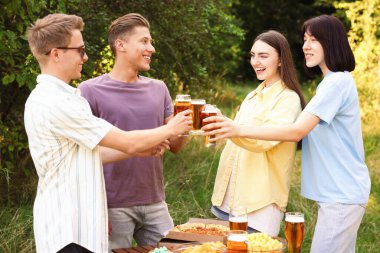 Bir grup mutlu arkadaş dışarıda bira bardaklarını tokuşturuyor.
