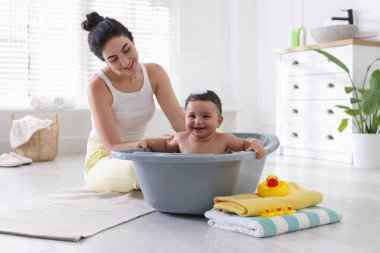 Anne küçük bebeğini evde yıkıyor.