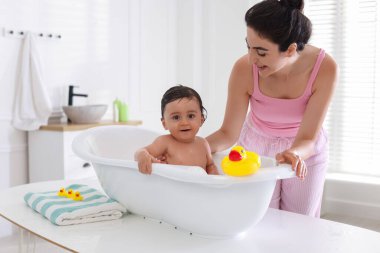 Anne küçük bebeğini evde yıkıyor.