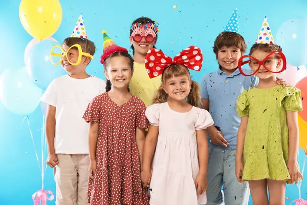 Doğum günü kutlaması. Açık mavi arka planda düşen konfeti altında neşeli dekorlu çocuklar.