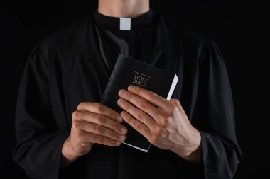 Siyah arka planda İncil 'i olan rahip, yakın plan.