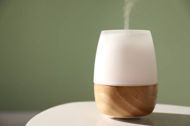 Yeşil duvara karşı beyaz masada şık bir aroma lambası, yakın plan. Metin için boşluk