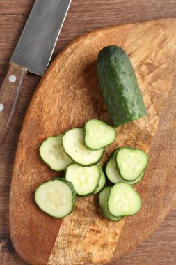 Tahta masanın üzerinde taze salatalık ve bıçak dilimleri var.