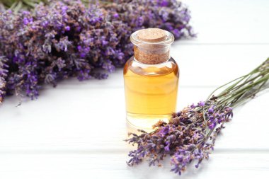 Lavanta yağı ve çiçekler beyaz ahşap masada, yakın plan.