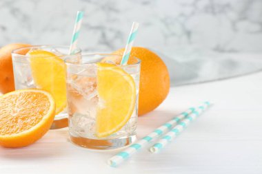 Bardaklarda portakal dilimleri ve beyaz ahşap masada taze meyveler olan köpüklü su, yakın plan. Metin için boşluk